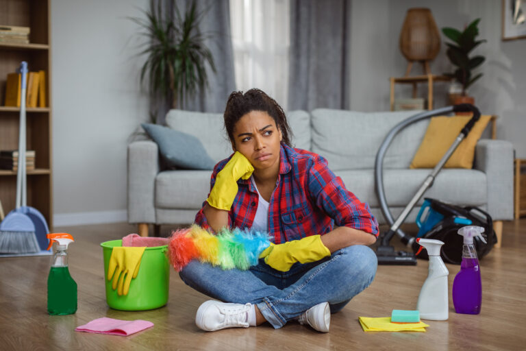 Boring thoughtful millennial african american housewife in rubber gloves with cleaning supplies sit on floor